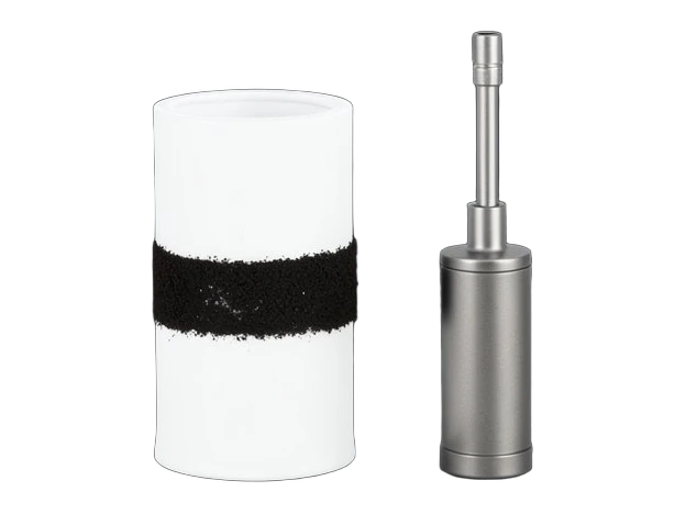 A white cylindrical air filter cartridge with a dark soot band standing upright beside a small metal air-sampling pump with a short intake tube.